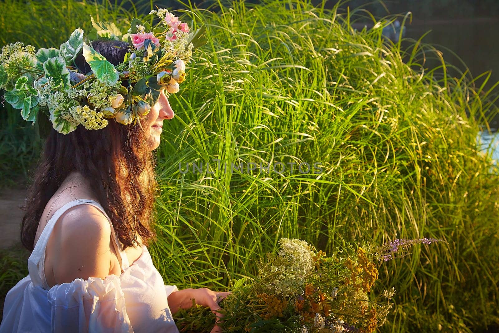 Slavic plump chubby girl in long white dress on the feast of Ivan Kupala with flowers and water in a river or lake on summer evening