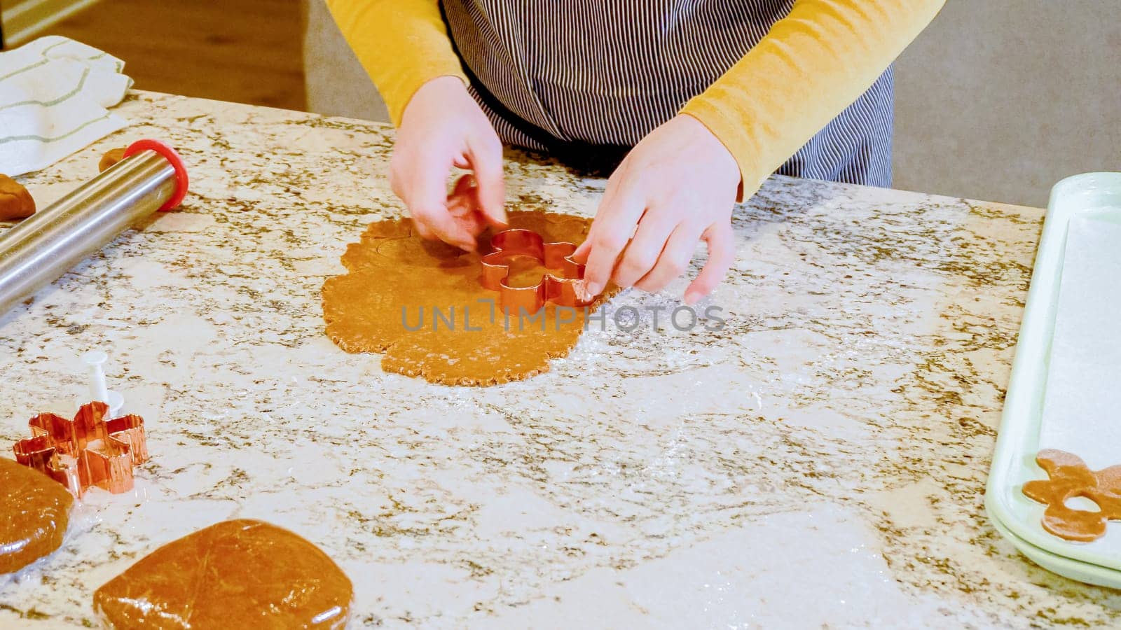 Using various festive cookie cutters, we're cutting out charming gingerbread cookies from the rolled dough on the sleek marble counter, bringing holiday cheer to the modern kitchen.