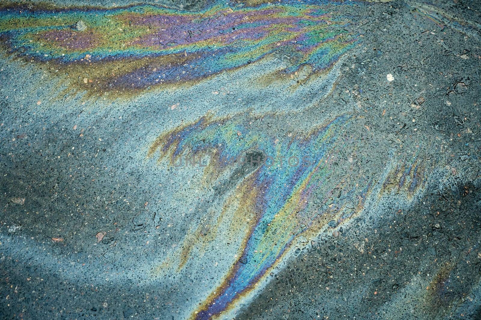 Rainbow-hued gasoline leak forming a colorful sheen on the dark surface of the asphalt road