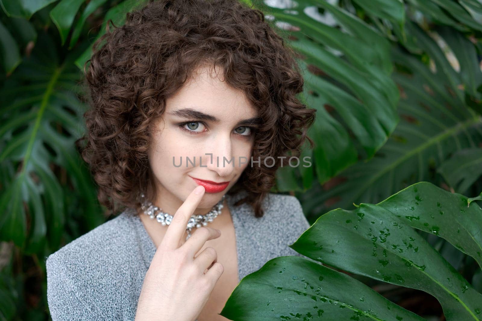 Woman with curly hair is posing for a picture. She is wearing a necklace and a red shirt