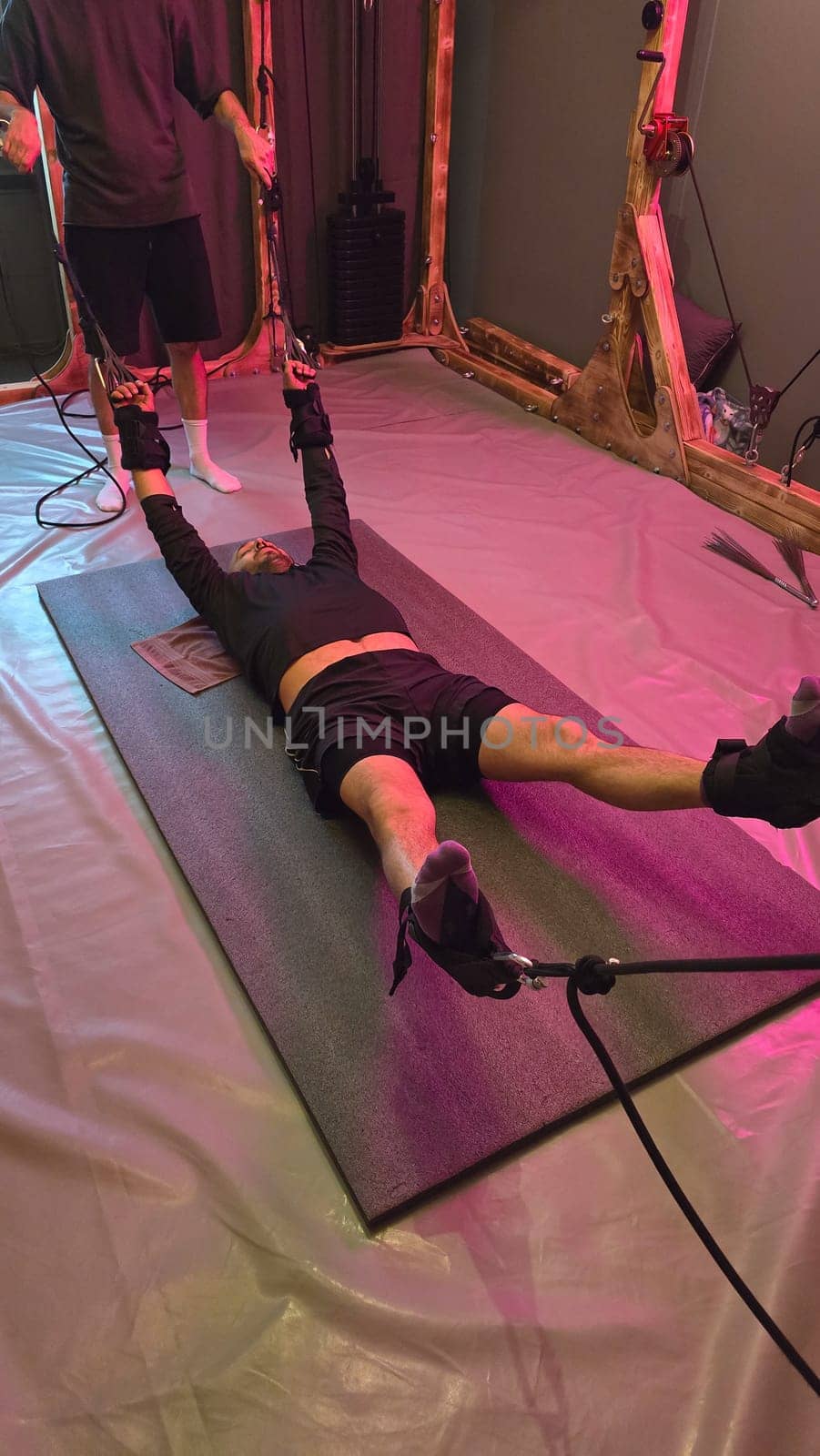 Male athlete exercising with suspension straps guided by personal trainer in modern neon lit gym
