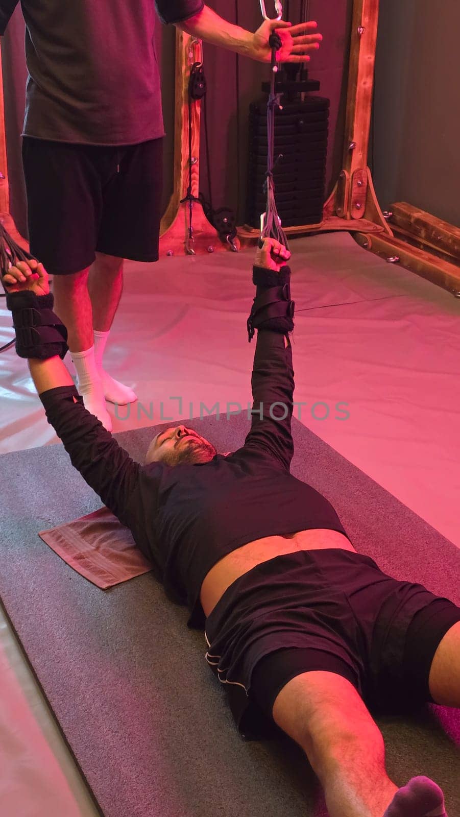 Male patient exercising on mat with elastic bands, assisted by healthcare professional, in rehabilitation center