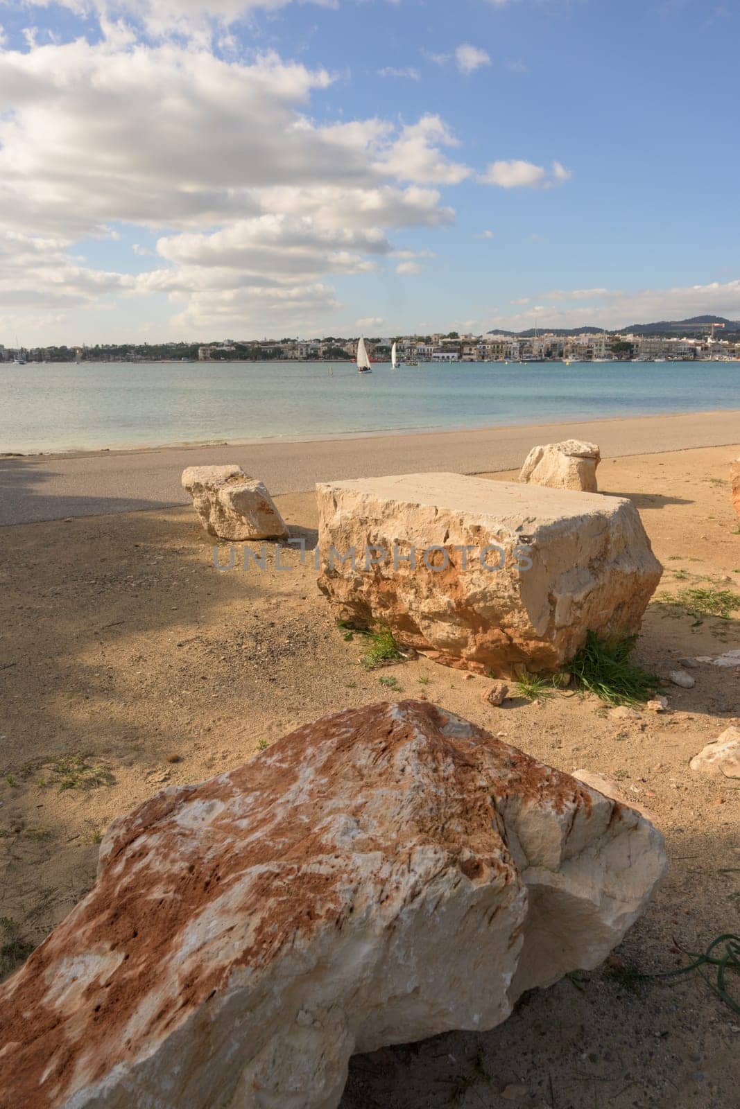 A serene beach with large rocks, calm waters and a town visible on the other side of the bay, portocolom.mallorca, balearic islands, spain