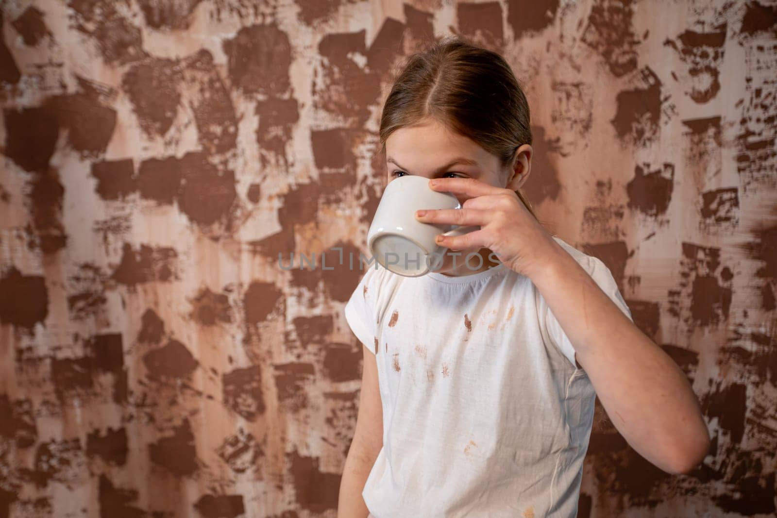 A young girl is happily sipping from a cozy mug, framed against a warm, earthy backdrop that inspires pure joy