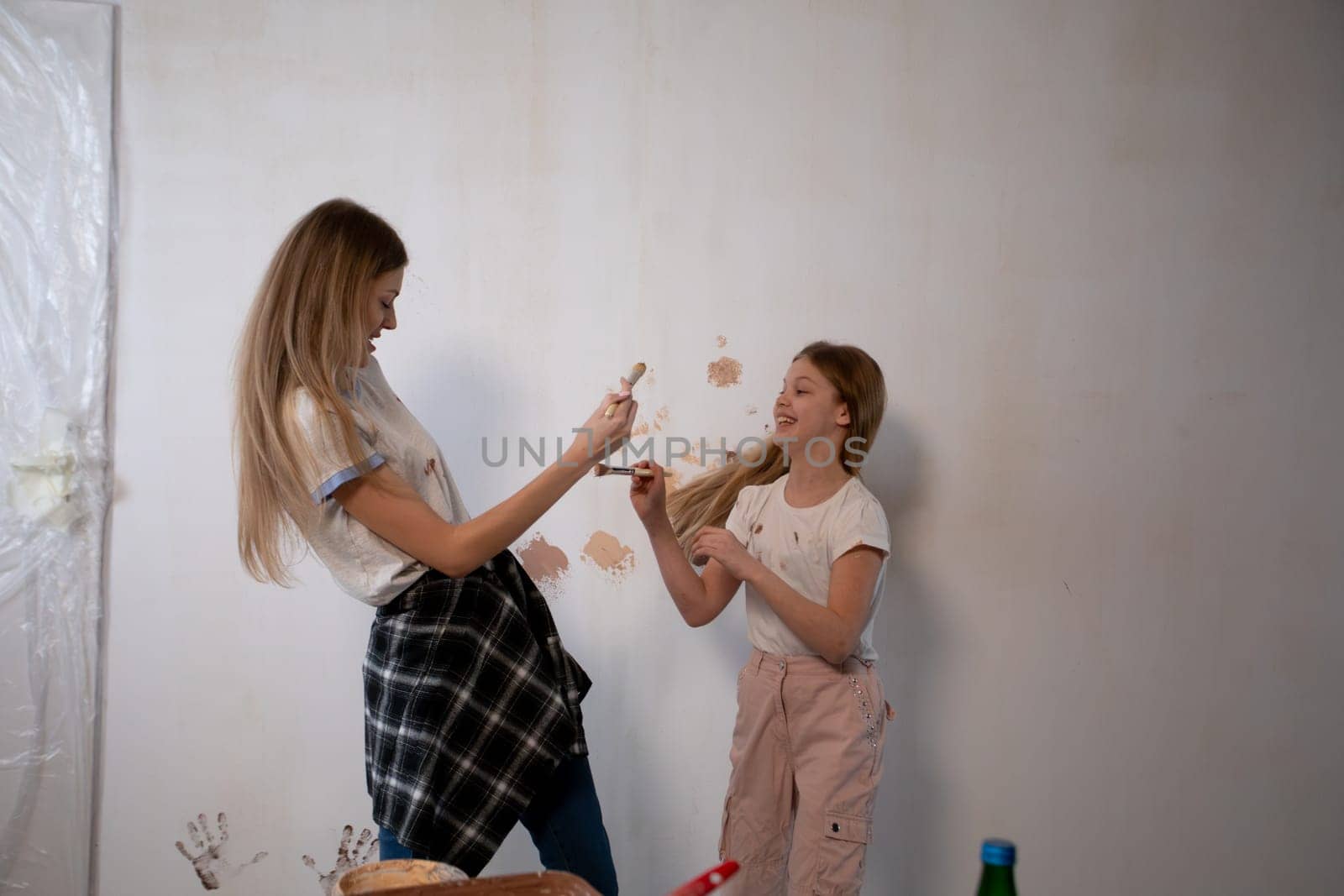 Two lively and playful girls joyfully engage in painting a wall together, as they bond and create lasting memories