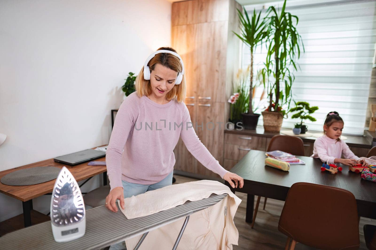 Woman listens to music while ironing clothes in a bright living space.