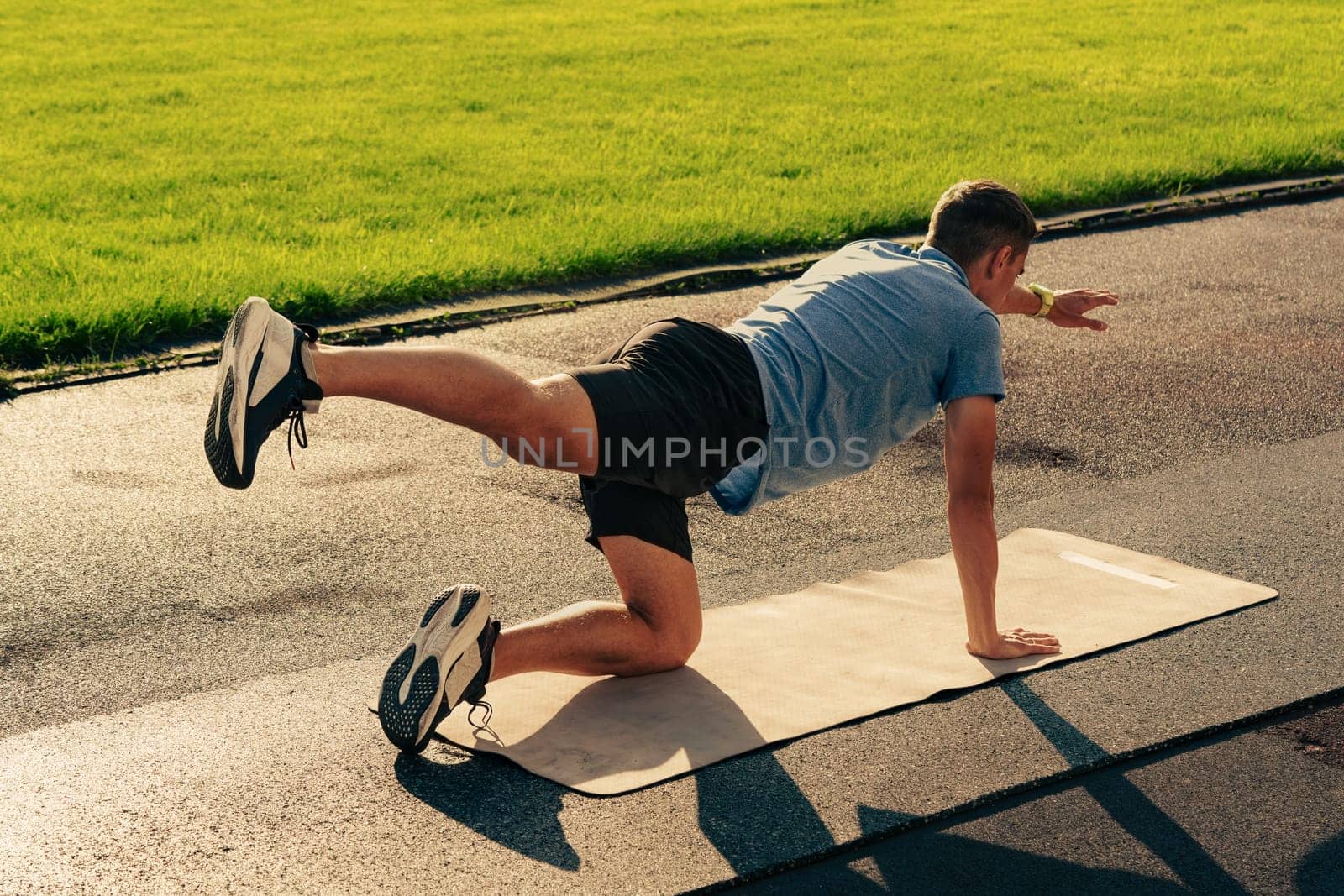 A person is engaged in a fitness activity on a mat in a sunny park. The individual demonstrates a workout pose, showcasing strength and balance against the green grass.