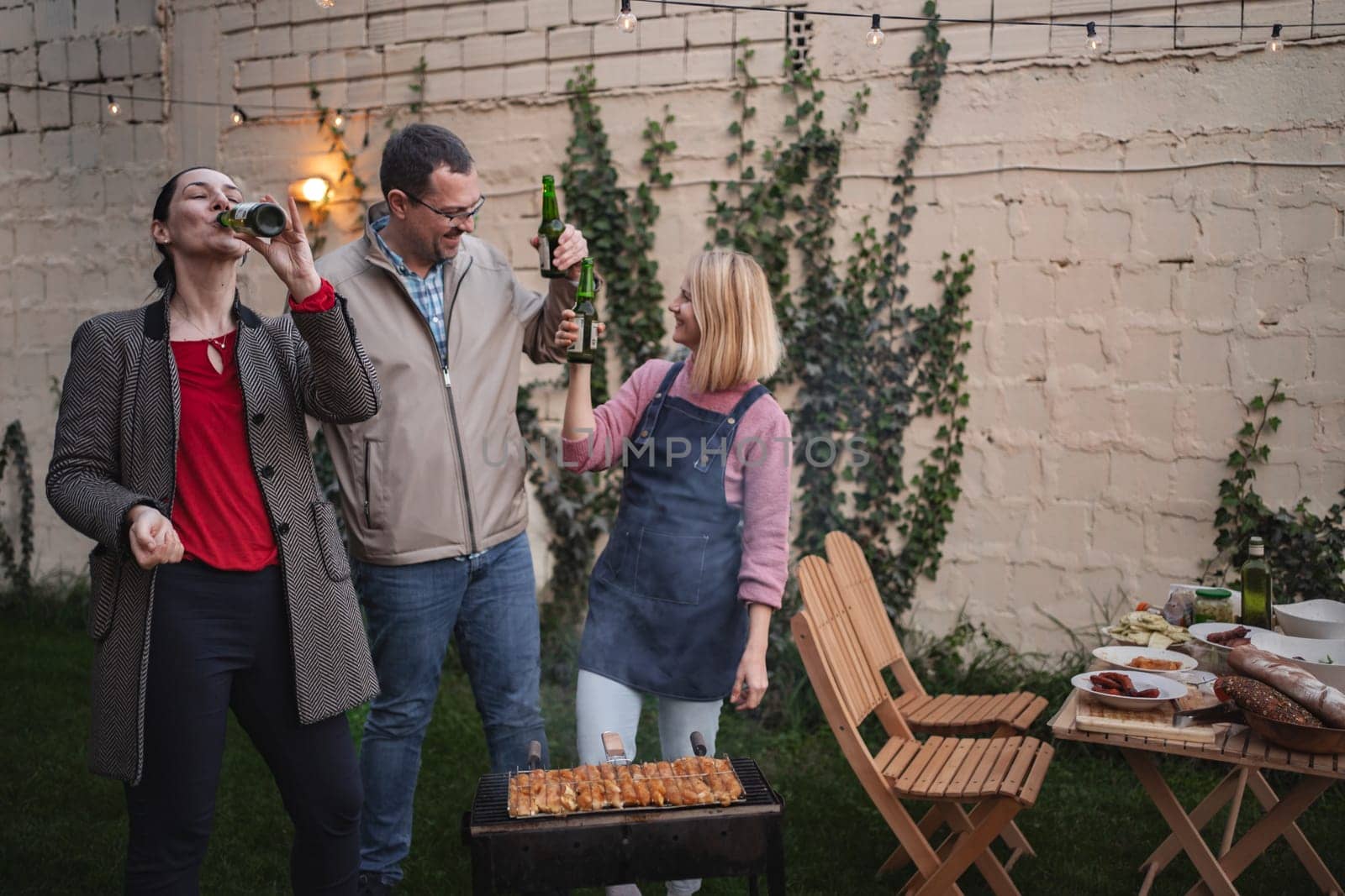 Three friends enjoy a lively barbecue together on a warm evening.