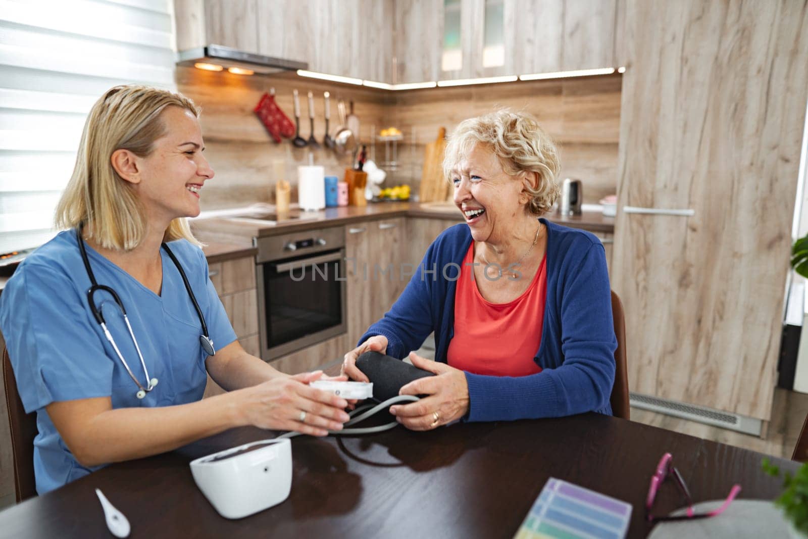 A nurse checks the blood pressure of an elderly woman in a warm kitchen.
