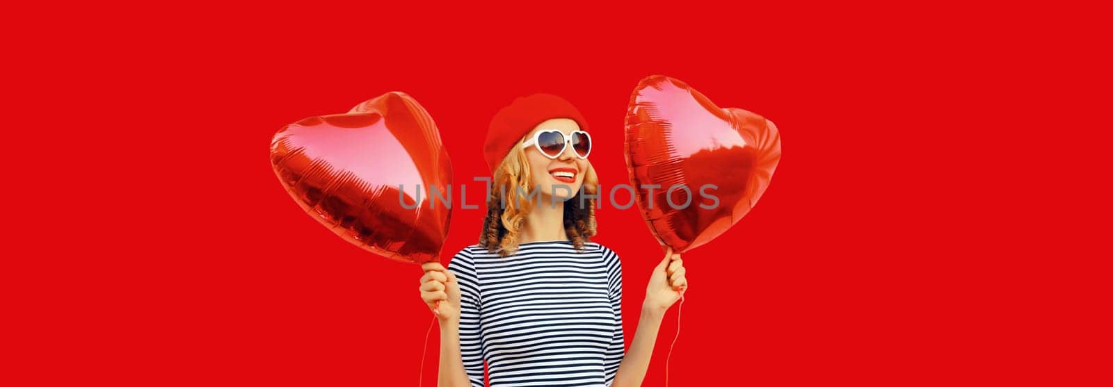 Portrait of happy joyful smile young woman holding red heart shaped balloon wearing french beret hat isolated on studio background