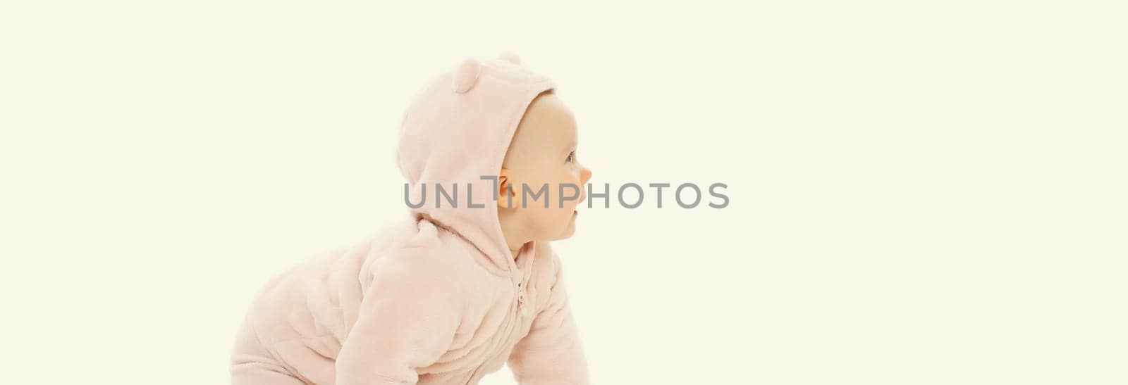 Happy cute baby in pink clothing crawling on the floor looking away on white studio background