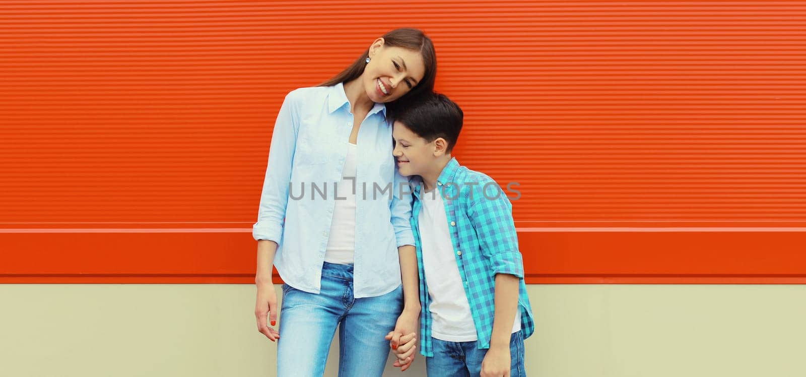 Happy smiling mother with son teenager together in casual clothing in the city on orange wall background