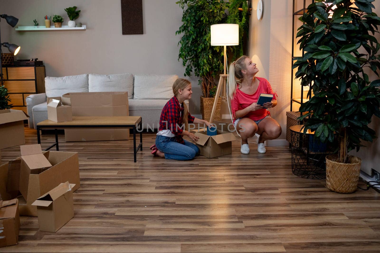 A mother and her child joyfully unpack boxes in their new home, surrounded by lush plants and ample natural light