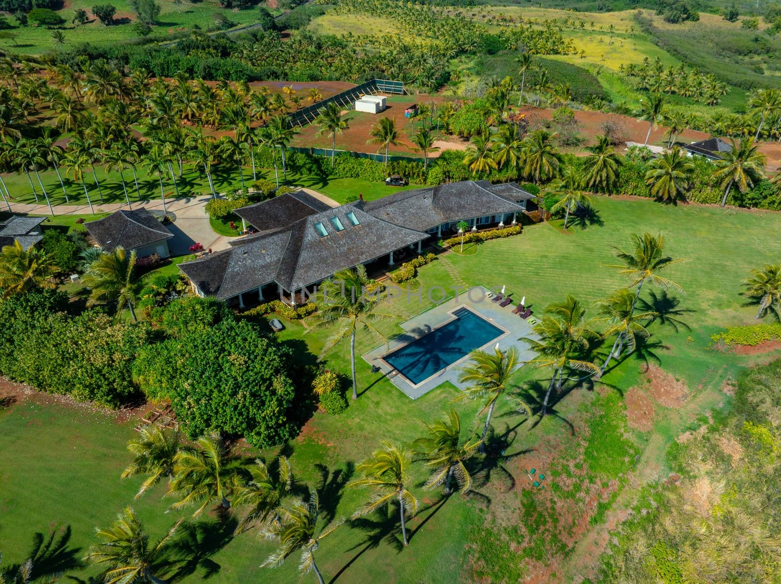 Aerial image of a modern house on Kauai Island, Hawaii, featuring a dark roof, skylights, a rectangular pool, manicured lawn, and lush greenery.
