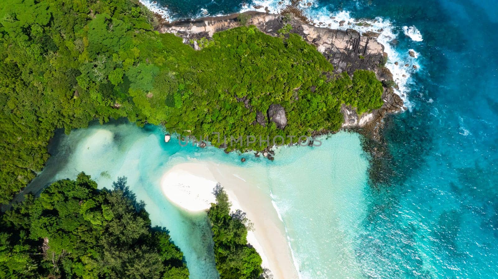 Lush greenery merges with crystal clear waters along the sandy beach on a sunny day. Grand Anse. Seychelles, Mahe.