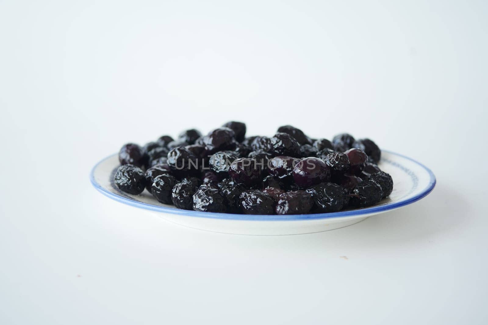 A plate filled with dried black olives sits on a plain background.