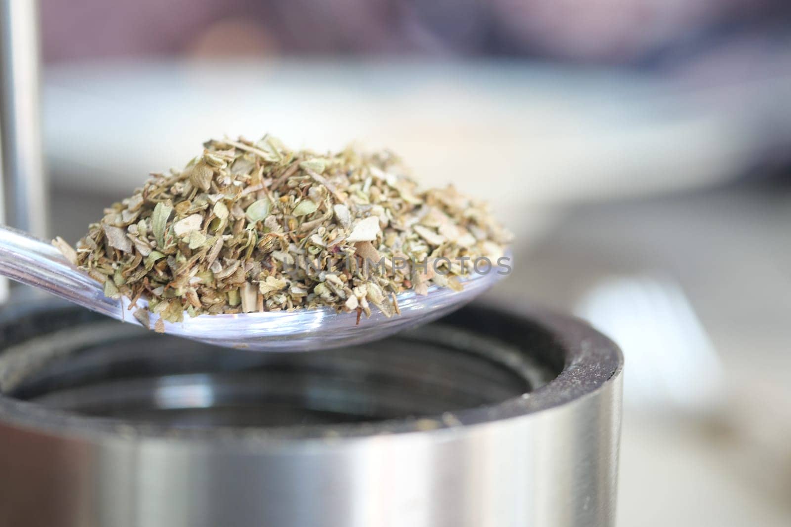 A close-up of herbs on a spoon above a metal container, ready for use.