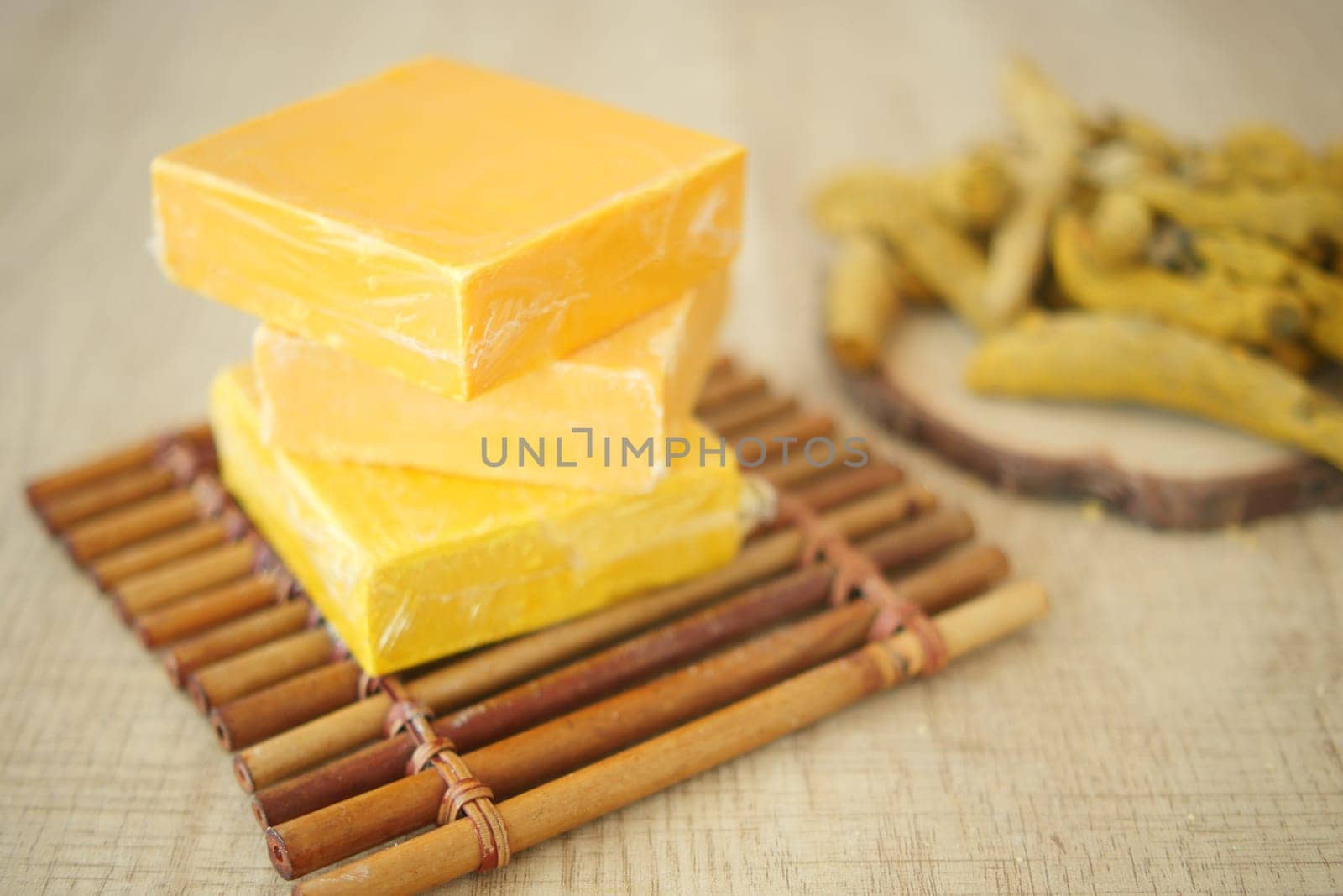 Yellow soap bars are neatly stacked on a bamboo mat beside dried herbs.