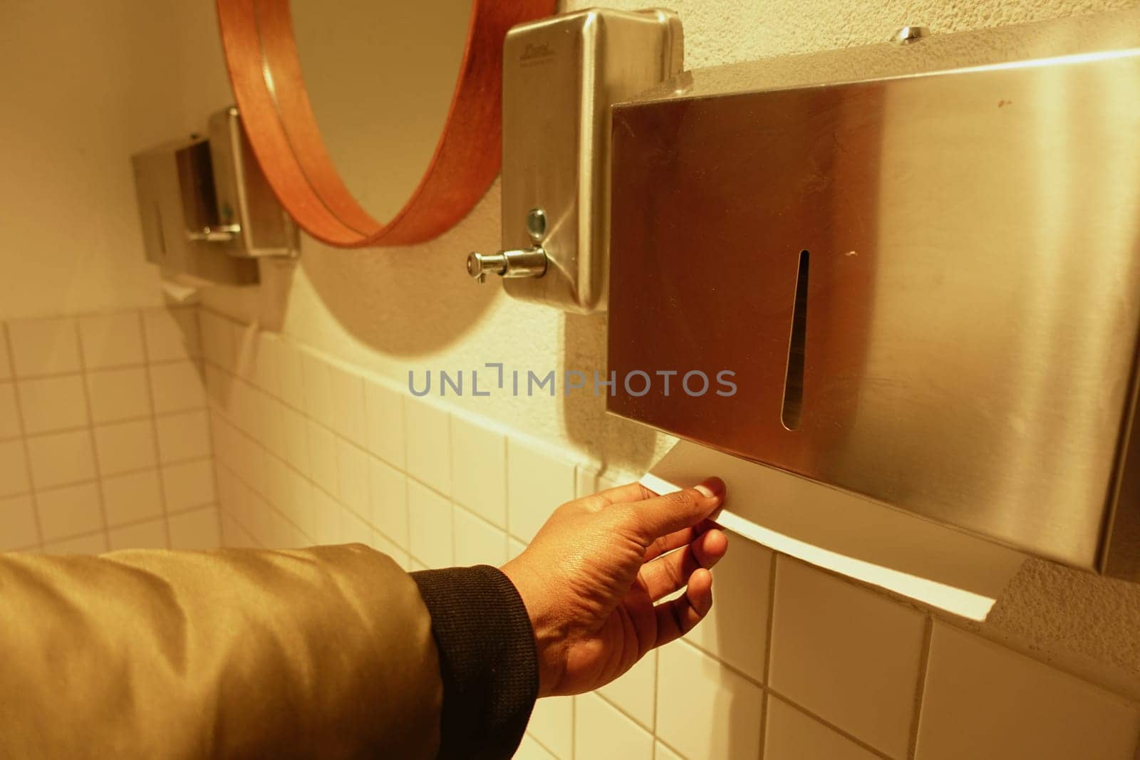 A person is grabbing a paper towel from a dispenser in a restroom.