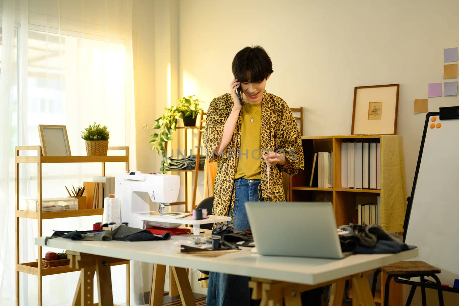 Smiling young designer having phone conversation in a creative fashion studio.