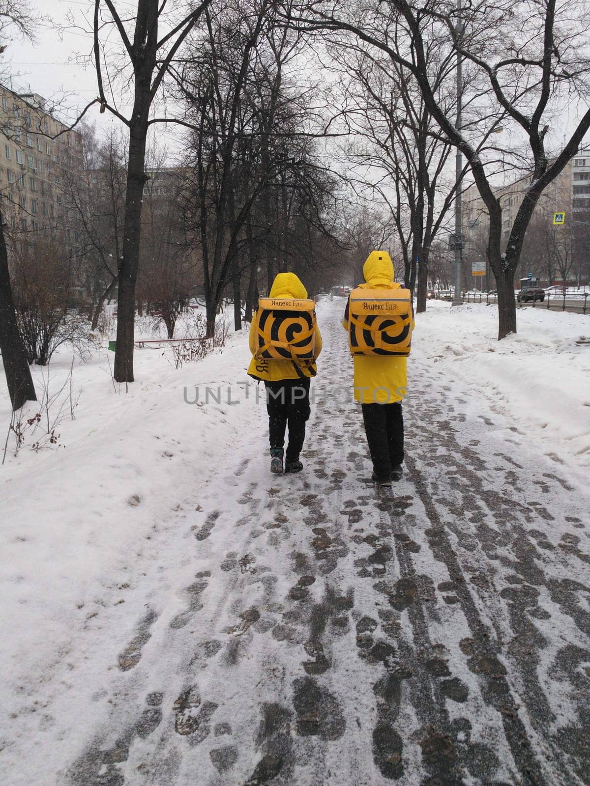 21.01.2019 Russia, Moscow. Couriers in yellow jackets walking in snowy urban park.