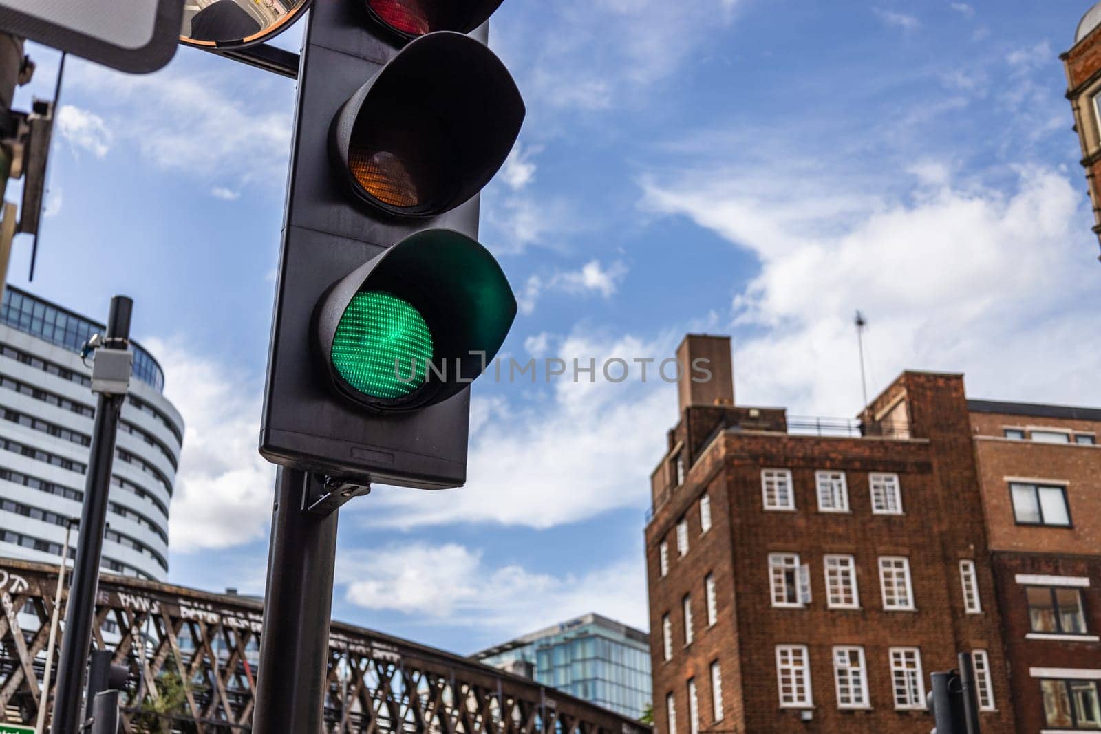 A green traffic light in an urban city setting, captured against a mix of modern and historic architecture under a blue sky