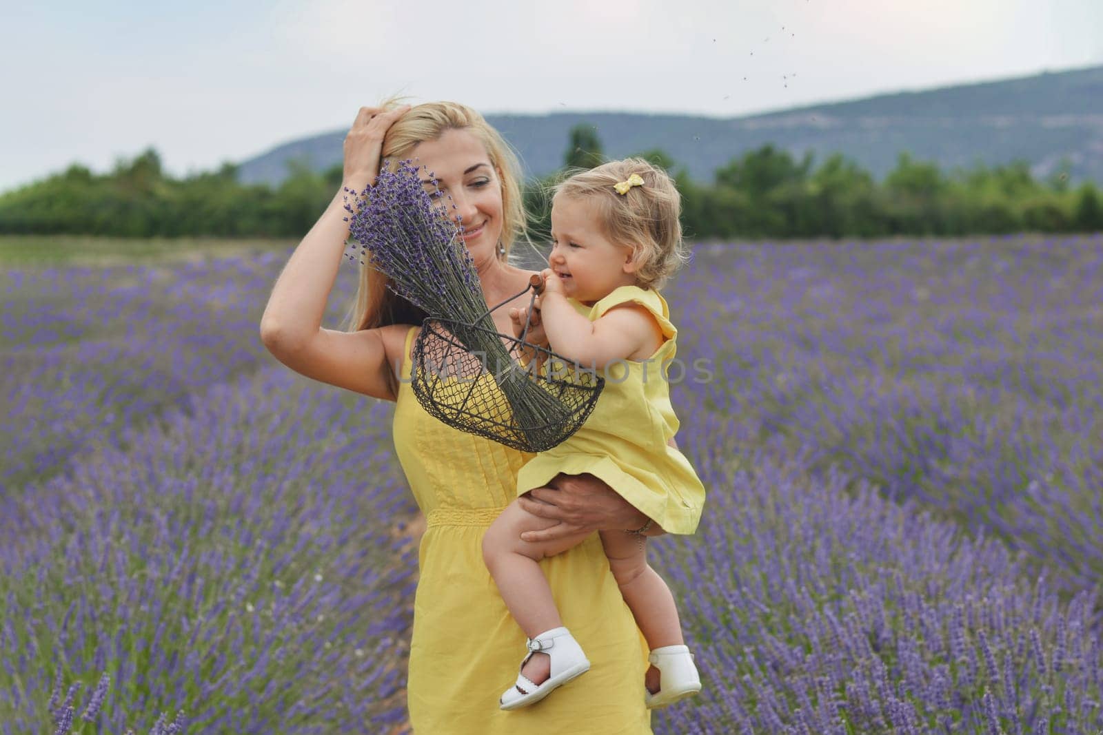 Mother and daughter in yellow dresses with basket and bouquet of lavender in lavender field in Provence France