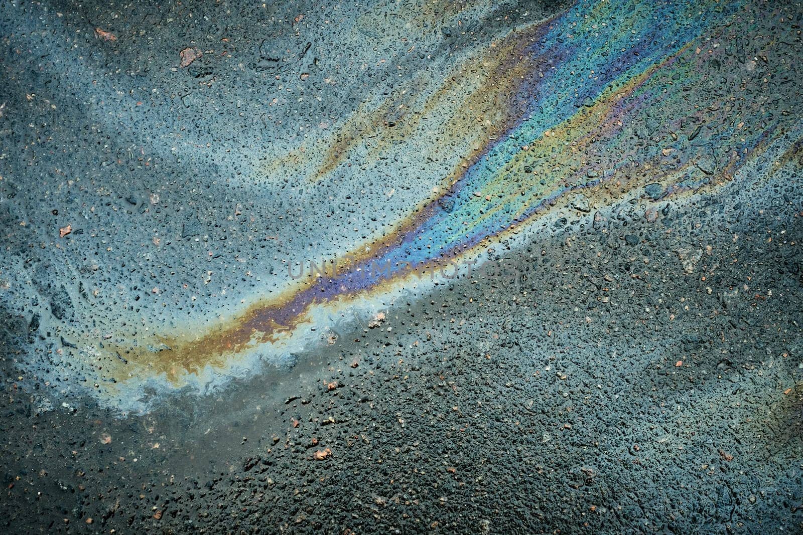 Moist asphalt in a parking lot, revealing an automotive oil spill