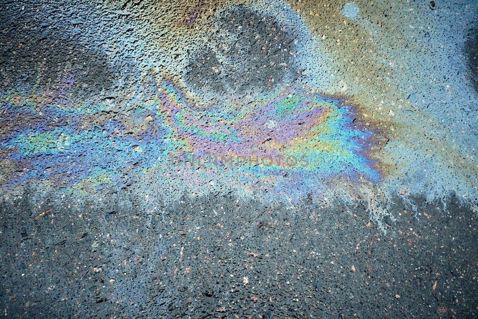 Up-close look at colorful oil patches, presenting a textured background filled with an array of tints on the road
