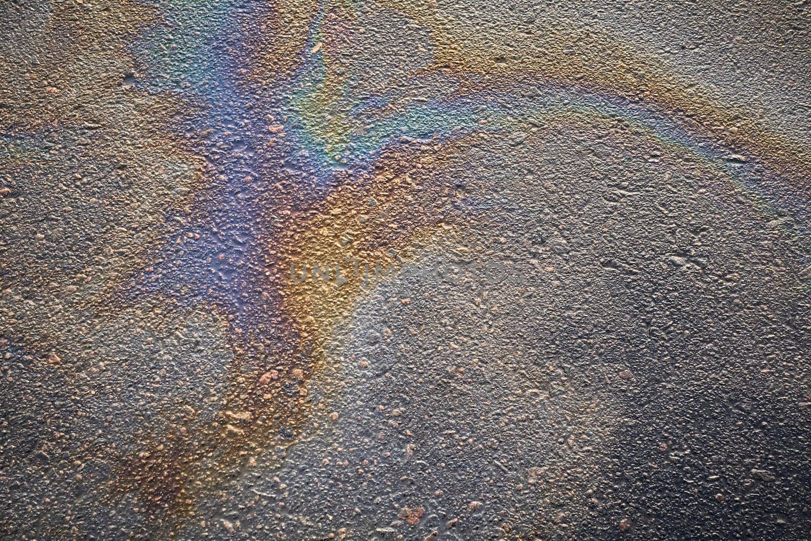 Colorful gasoline stains viewed up close, presenting a textured background with a variety of hues on the pavement road