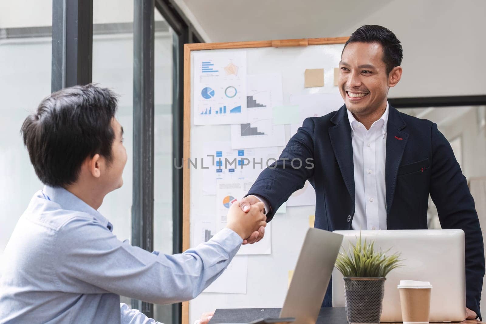 Two happy professional businessmen shaking hands after a successful financial deal at a meeting. by wichayada