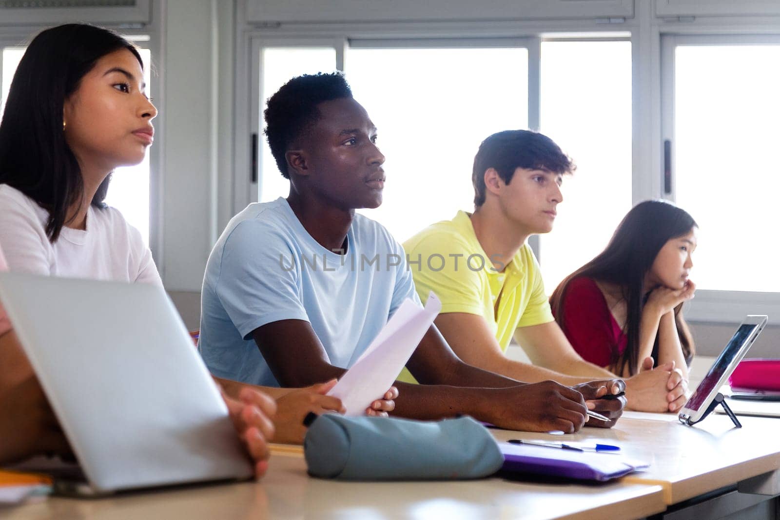 Black teen high school student in class listening to lecture with multiracial classmates. Focus on african american boy. by Hoverstock