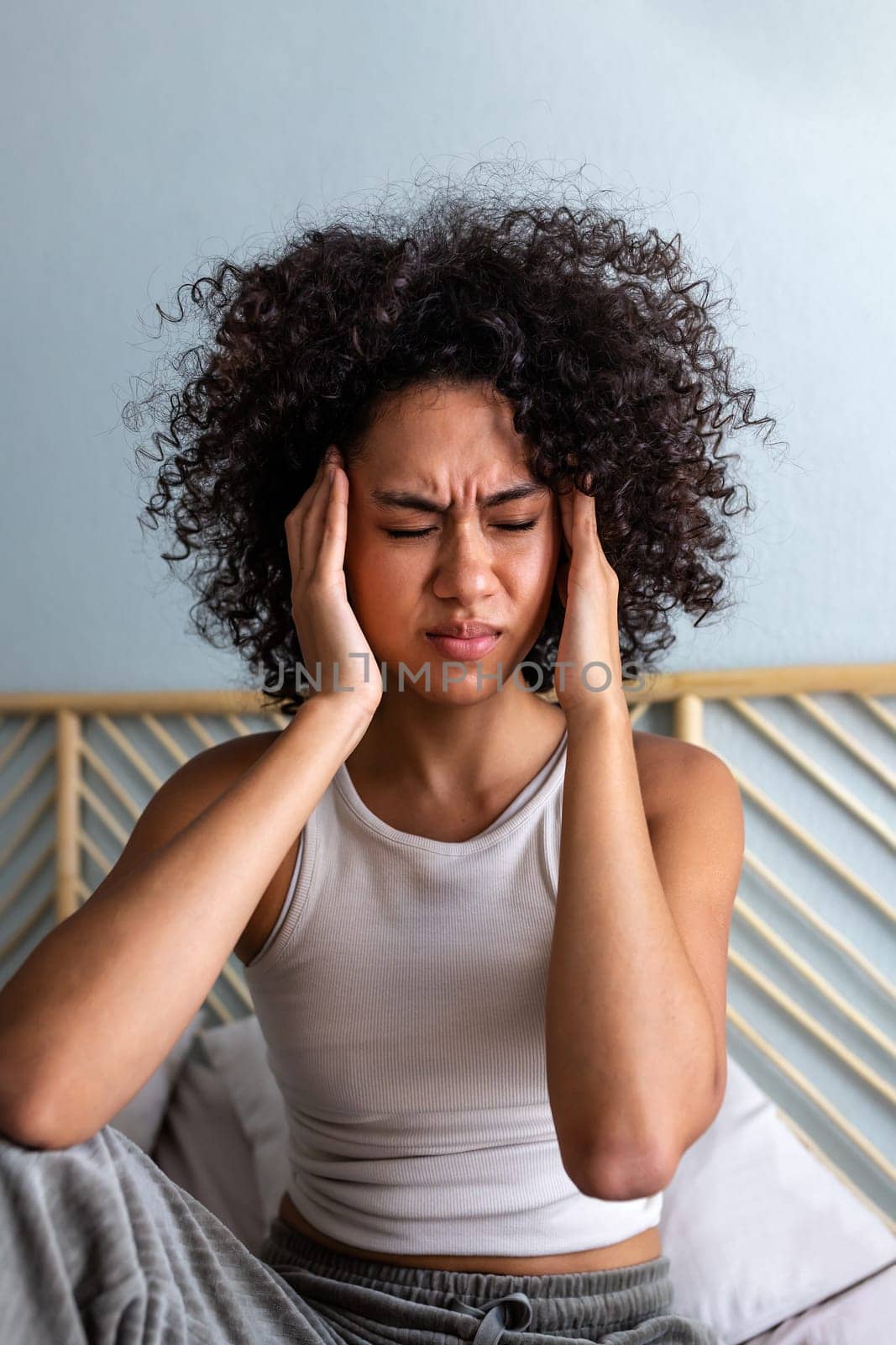 Vertical portrait of young African American woman touching temples and frowning having headache at home. Wellbeing by Hoverstock