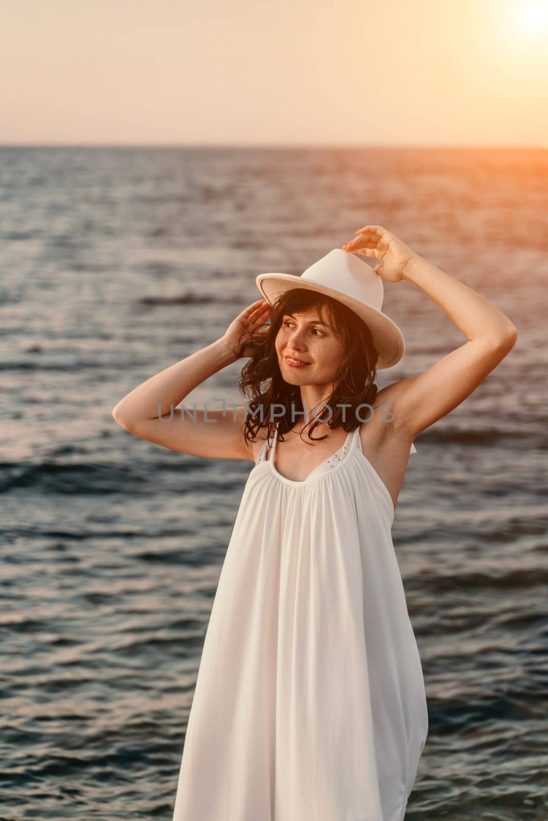 woman sea sunset. A woman in a dress, hat and with a straw bag is standing on the beach enjoying the sea. Happy summer holidays. by Matiunina