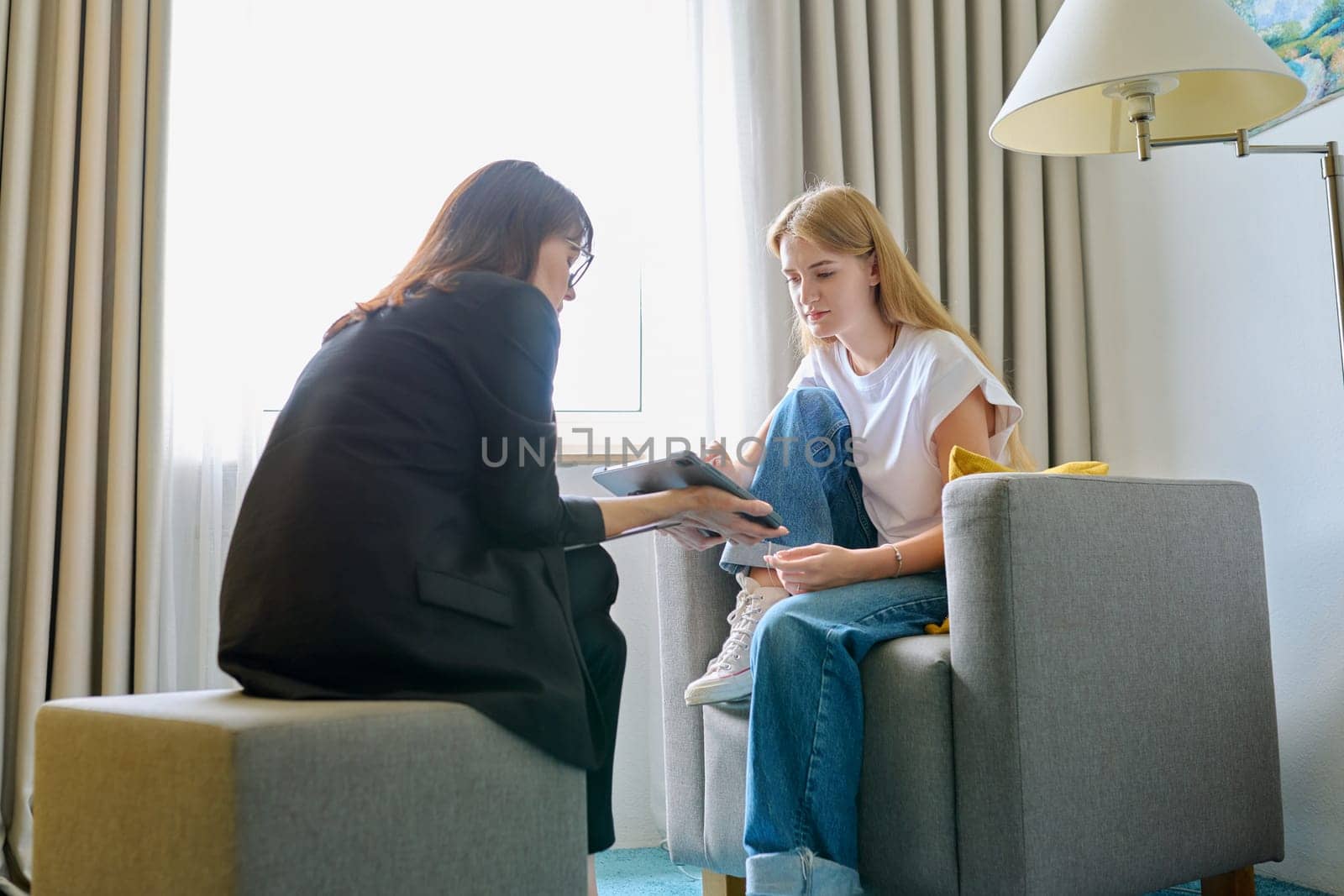 Young female at therapy meeting with psychotherapist. Session of teenage student girl, specialist psychologist with digital tablet talking to patient. Psychology, psychotherapy, treatment, youth mental health