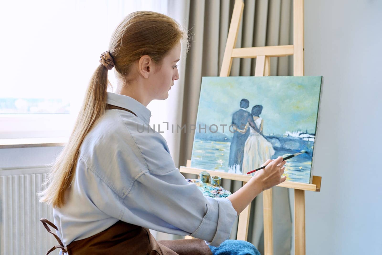 Young pretty female artist painting with acrylics on an easel by VH-studio