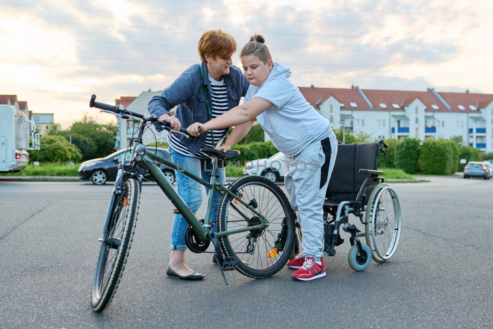 Boy transfers from wheelchair to bicycle, mother helping child to transfer, activity rehabilitation health concept
