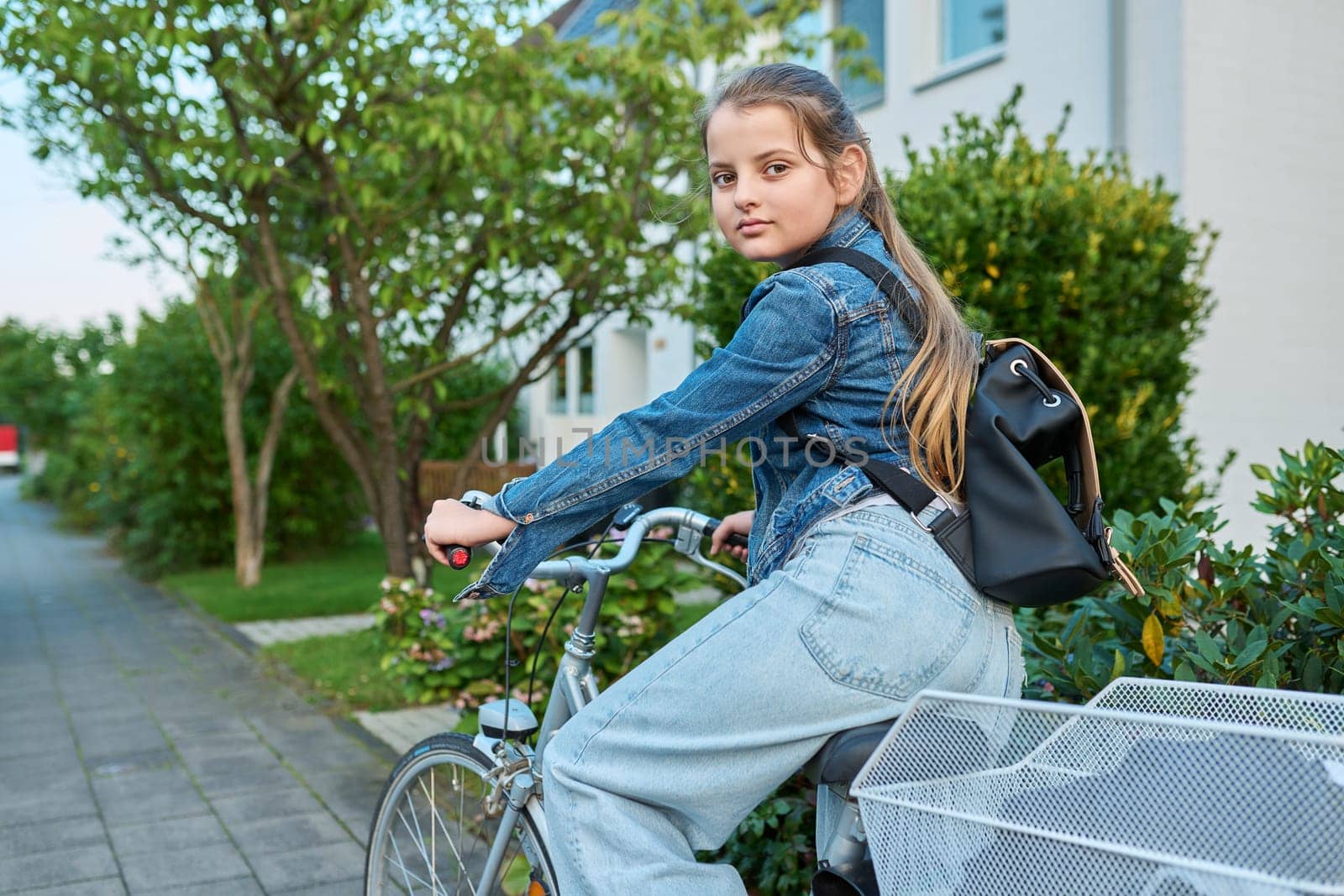 Back to school. Girl child 10, 11 years old with backpack on bicycle on street near house, posing looking at camera. Schoolgirl cycling to school, lifestyle, childhood concept