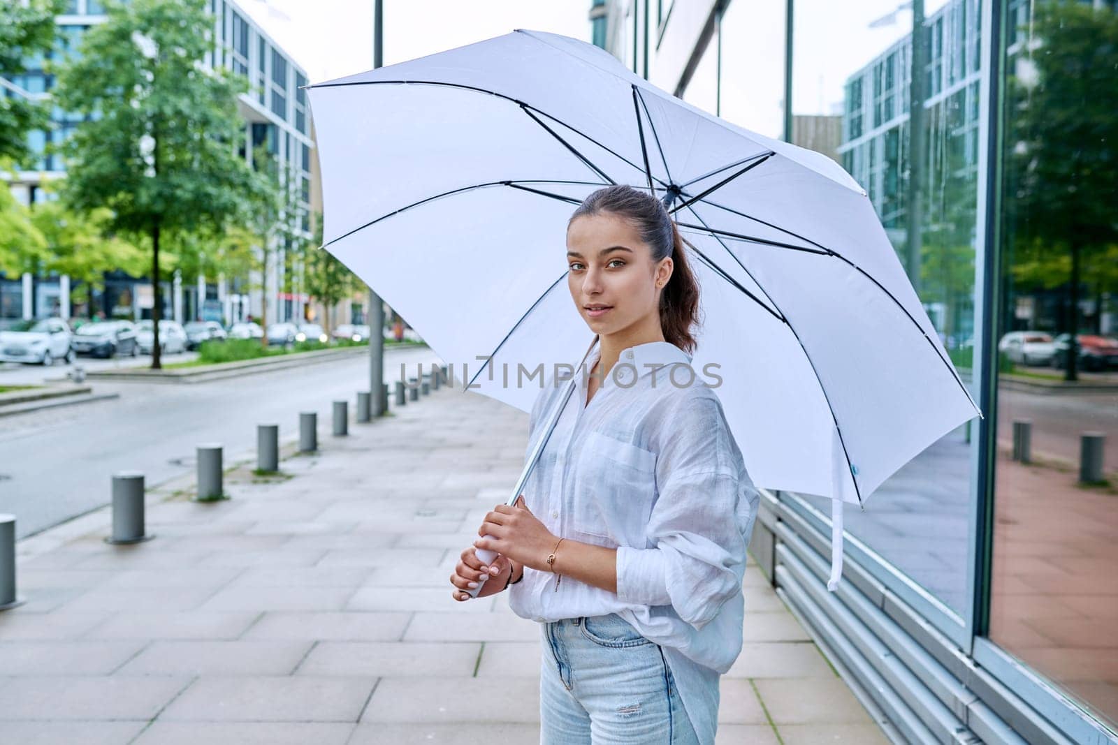 Young teenage female on a summer cloudy day under a white umbrella on a city street