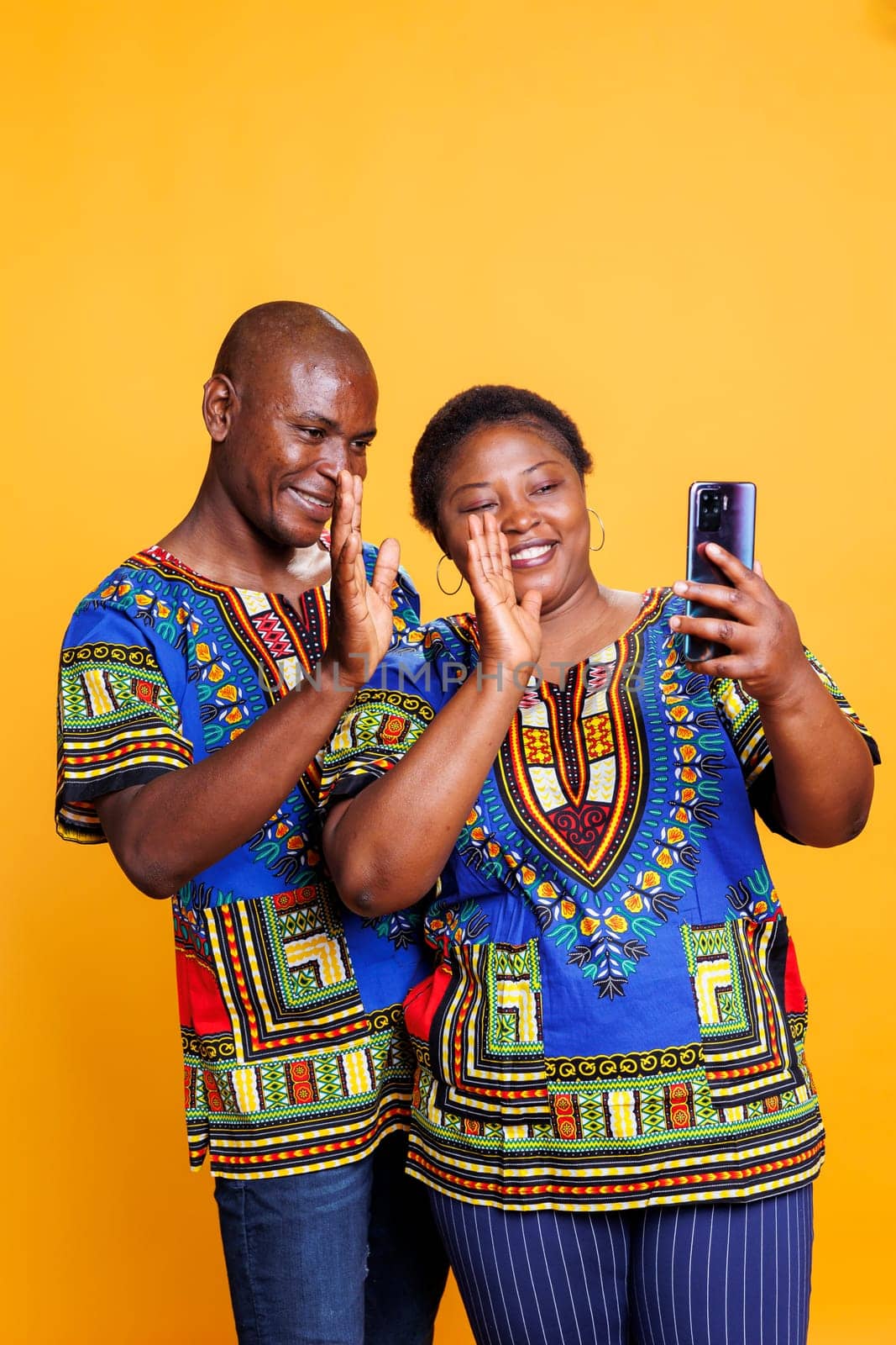 Smiling man and woman greeting and waving hello while having online call on smartphone together. Cheerful happy couple holding mobile phone and speaking in remote videocall