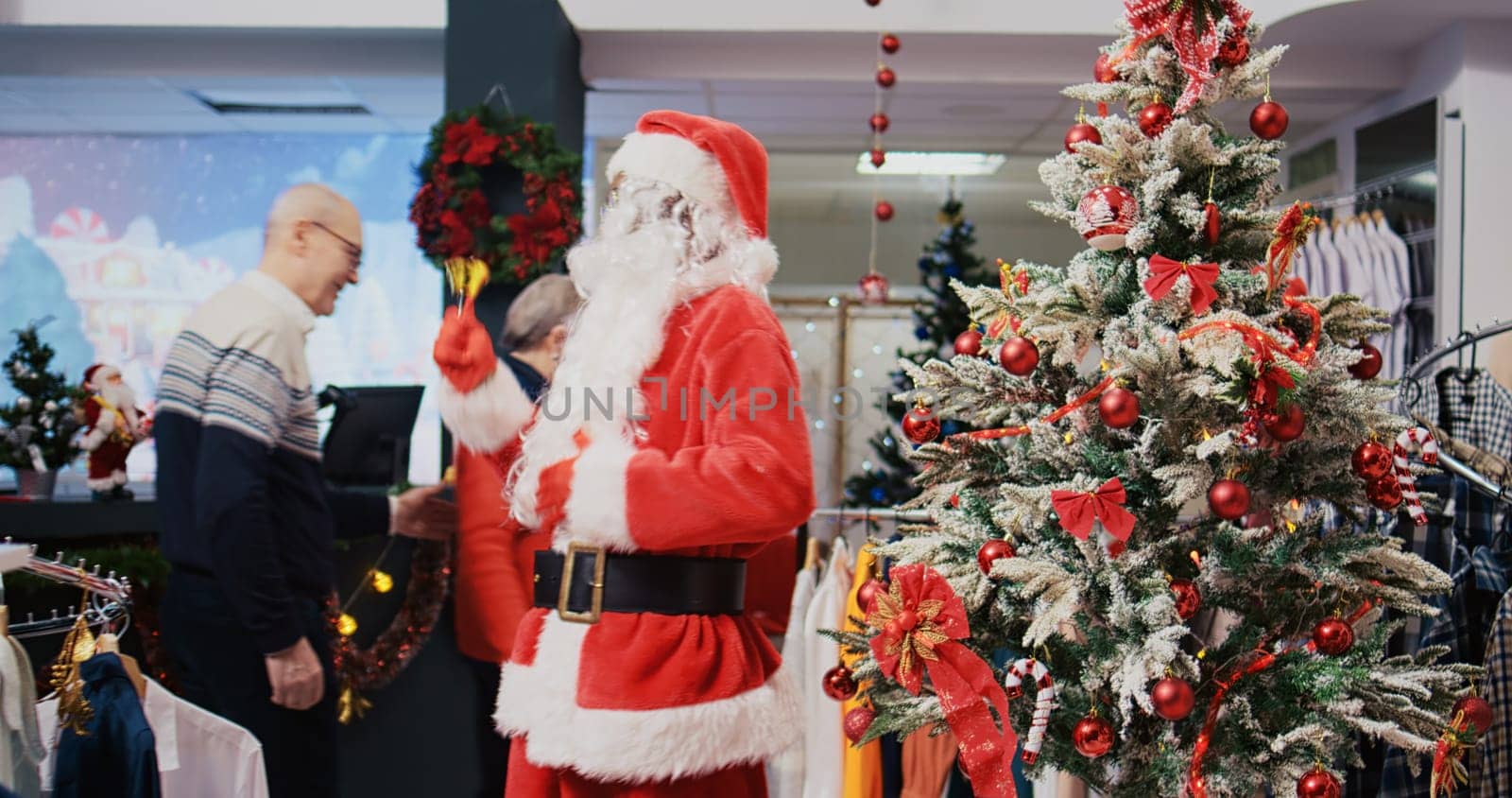 Joyful african american worker dressed as Santa Claus in Christmas ornate shopping mall clothing shop. Employee jingling xmas bells and greeting happy clients in festive adorn fashion store
