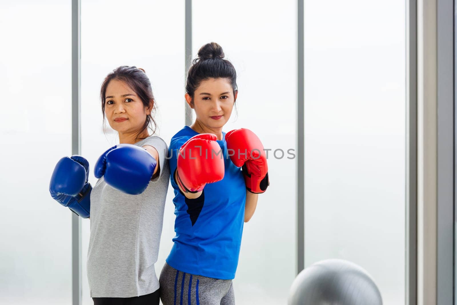 Asian lifestyle adult and young woman smiling sports fitness boxer wearing gloves practicing kick on boxing in sportswear work out indoor yoga studio, sport healthy workout concept