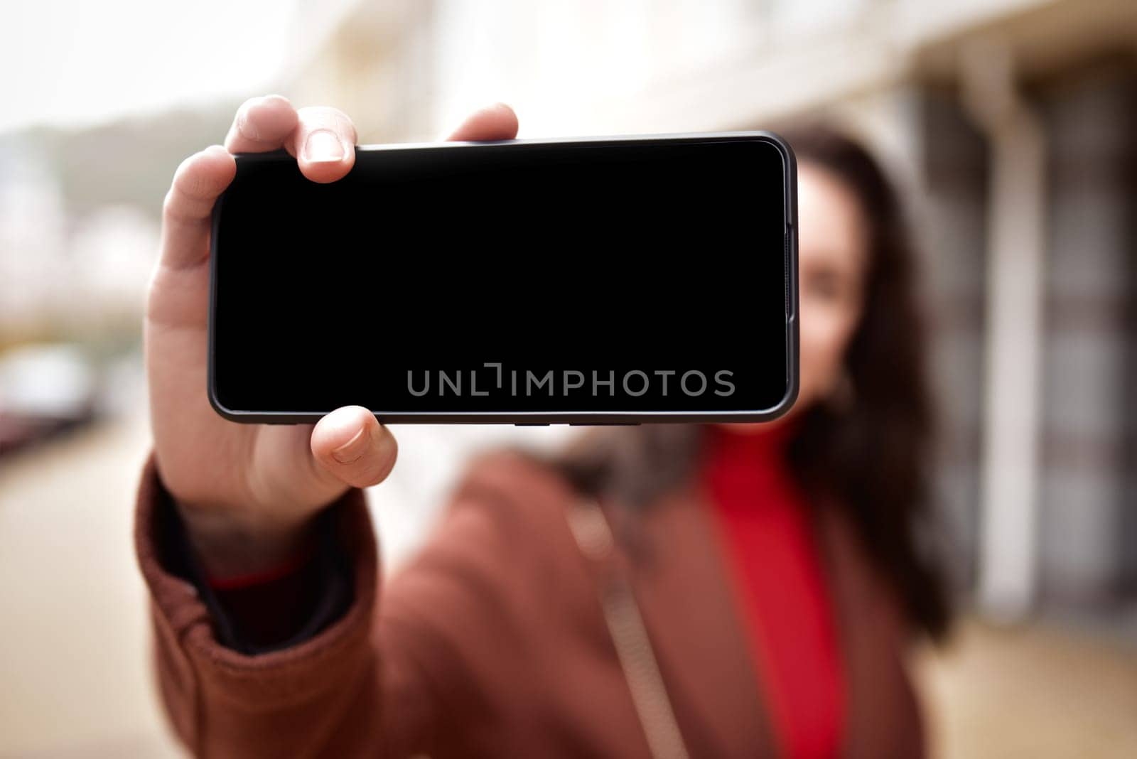 young woman taking selfies walking down the street, holding a smartphone with a black screen.blank screen by Nickstock