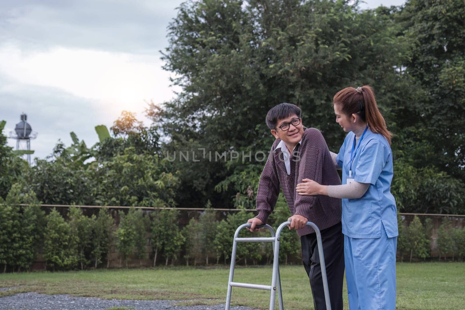 Asian woman caregiver helping senior man walking. Nurse assisting he old man patient at nursing home. Senior man using walker being helped by nurse at home. Elderly patient care and health lifestyle by wichayada