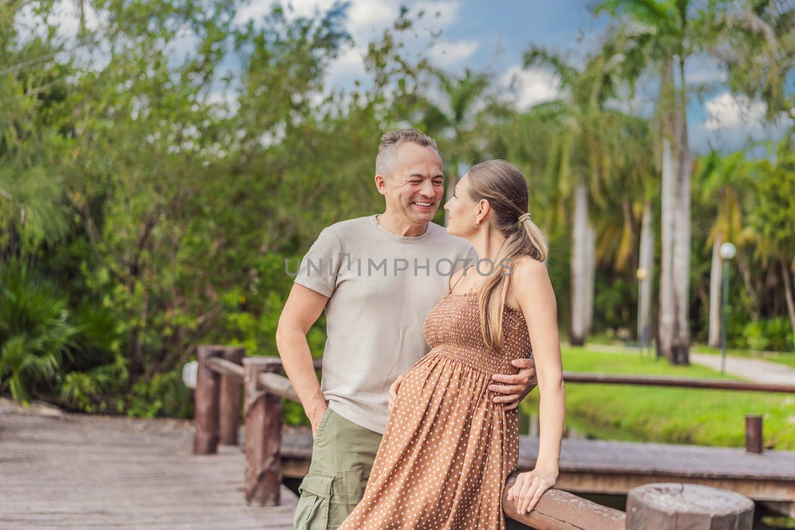 A happy, mature couple over 40, enjoying a leisurely walk in a park, their joy evident as they embrace the journey of pregnancy later in life.