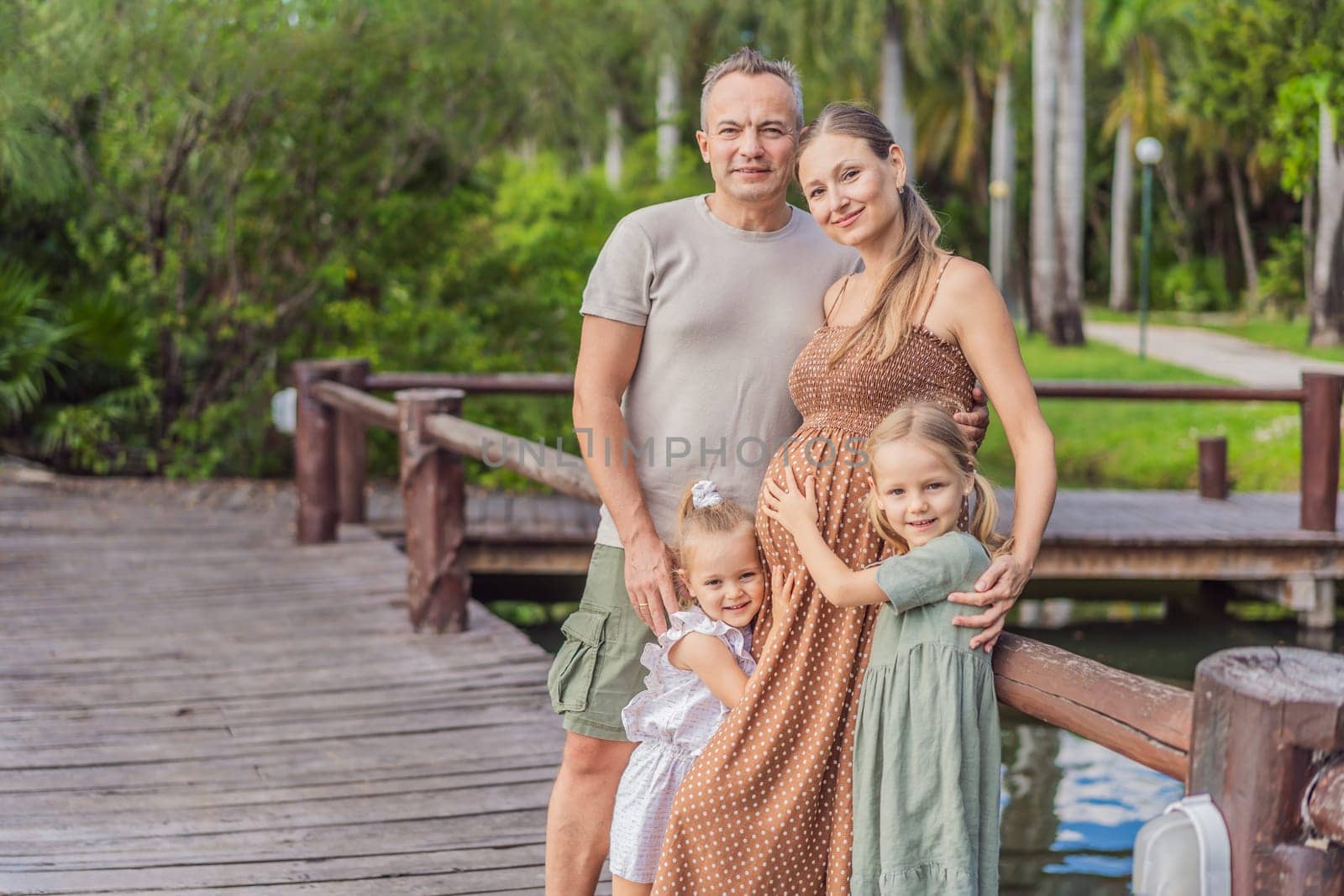 A happy, mature couple over 40 with their two daughters, enjoying a leisurely walk in a park, their joy evident as they embrace the journey of pregnancy later in life.