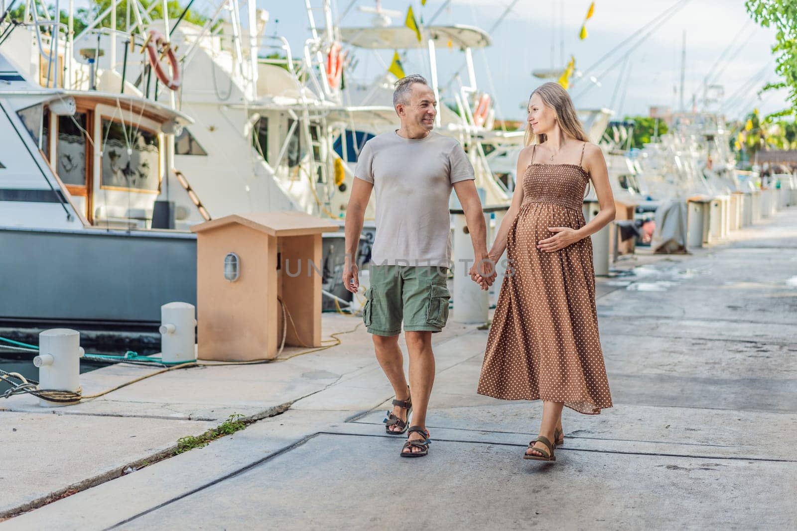 A happy, mature couple over 40, enjoying a leisurely walk on the waterfront, their joy evident as they embrace the journey of pregnancy later in life.