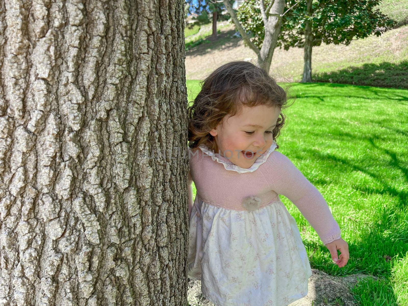 Cute little girl is playing around the grass and trees at the park