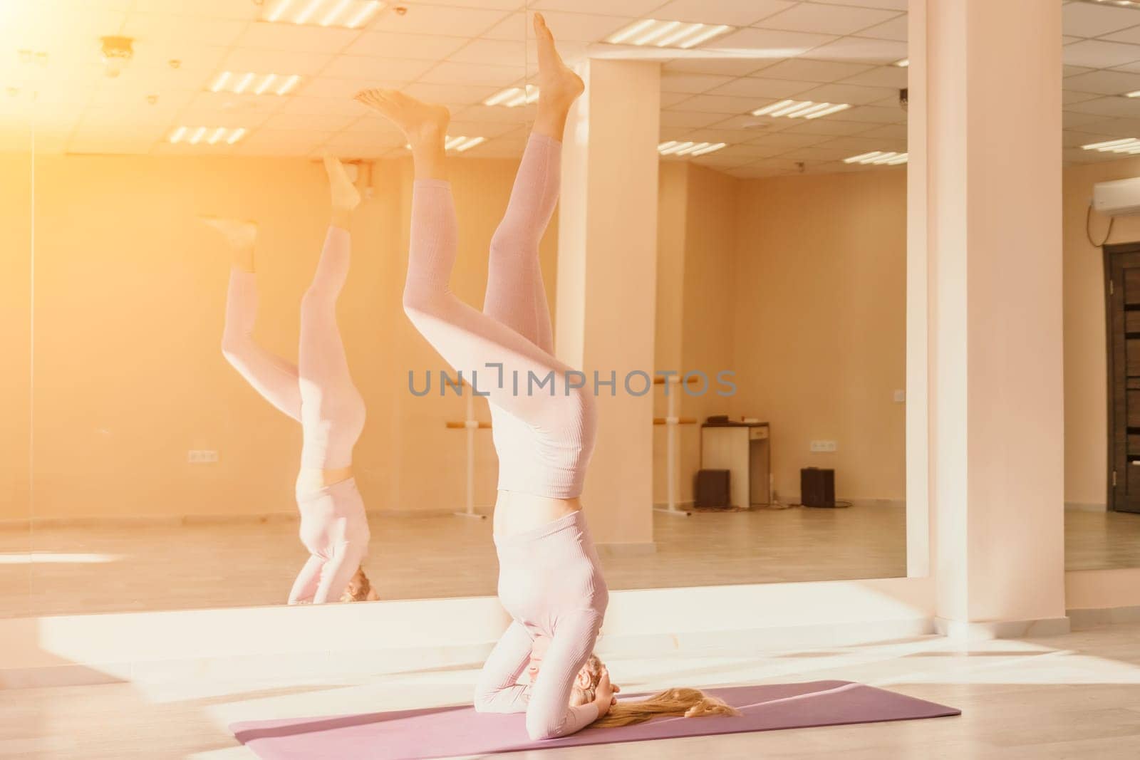 Young sporty woman, fitness instructor in pink sportswear doing stretching and pilates on yoga mat in the studio with mirror. Female fitness yoga routine concept. Healthy lifestyle and harmony. by panophotograph