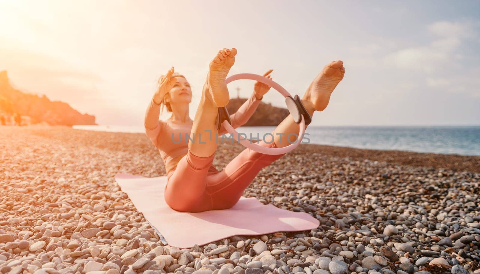 Woman sea pilates. Sporty happy middle aged woman practicing fitness on beach near sea, smiling active female training with ring on yoga mat outside, enjoying healthy lifestyle, harmony and meditation by panophotograph